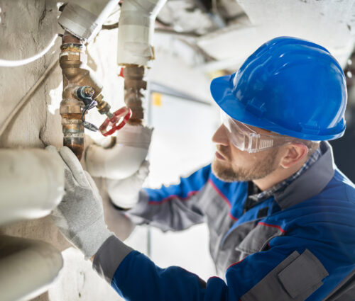 Male Worker Inspecting Water Valve For Leaks In Basement